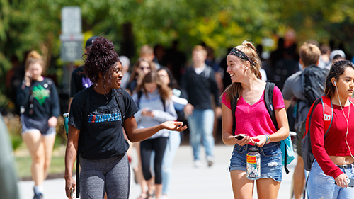 Two female students talking while walking to class on a sunny day.
