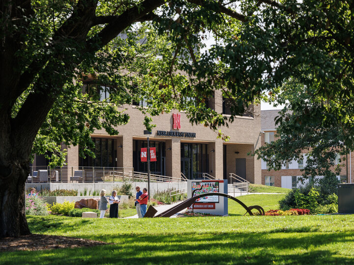 Four people stand and talk outside the East Campus Union on a sunny day