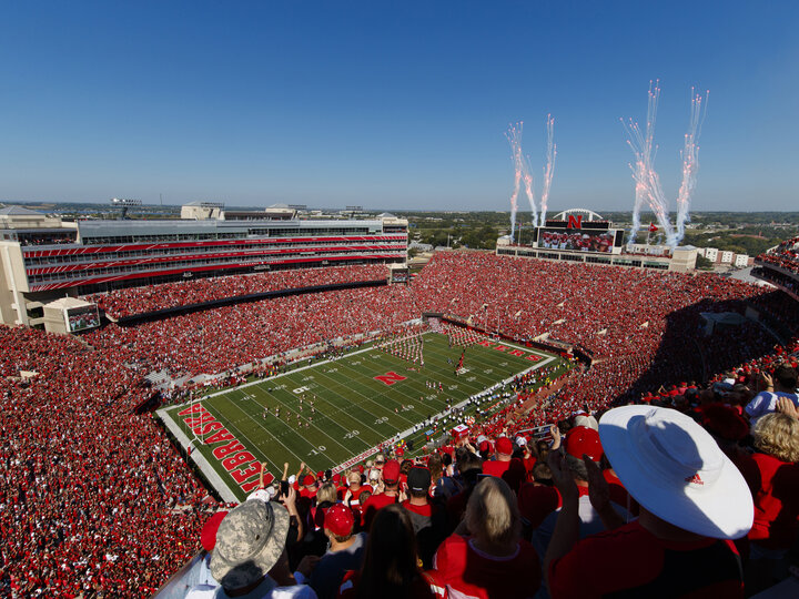 Fireworks explode in a clear, blue sky as fans cheer on the Husker football team as seen from the top of Memorial Stadium.