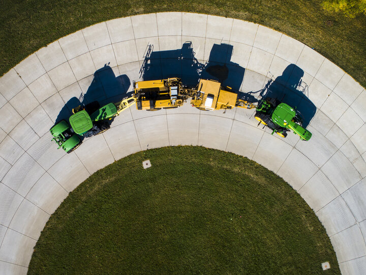 Aerial view of a green tractor pulling a yellow test car (yellow) and an additional tractor for weight as it rounds the test track on East Campus