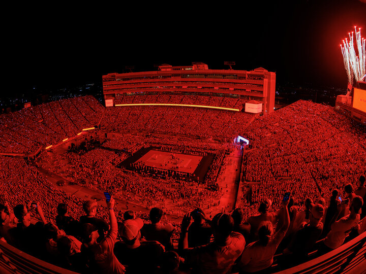 92,003 fans are bathed in red light at Memorial Stadium as fireworks soar high in the nighttime sky for Volleyball Day in Nebraska.