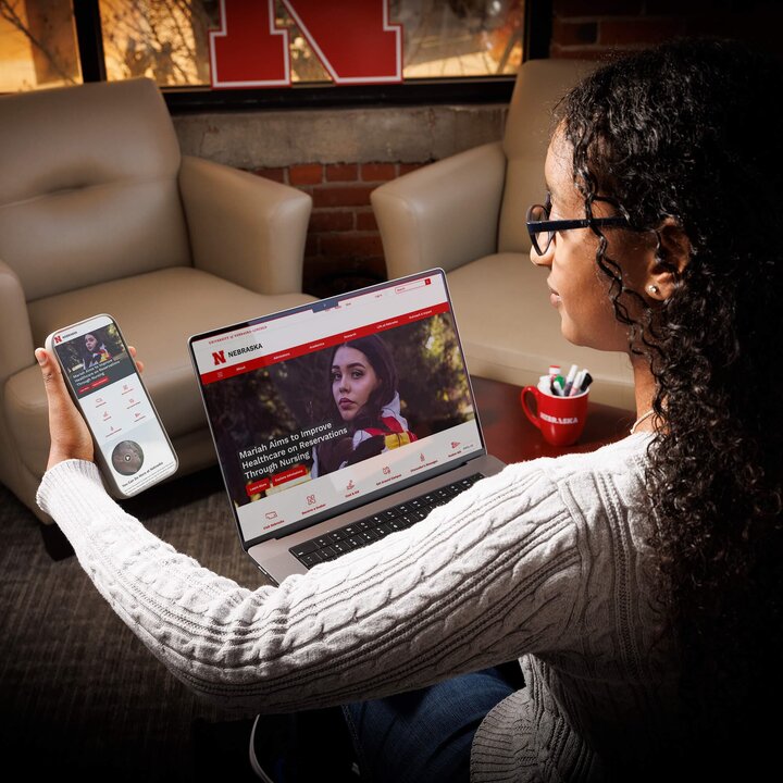 An intelligent woman looking at the UNL top level website on her phone and laptop.